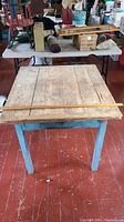 Full front view of the table showing the blue frame and natural pine top with a measuring stick laid across for scale.