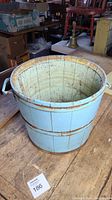 Blue wooden bucket viewed from the side, showing two metal handles and old paint.