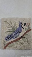 Full view of the square table mat showing the bluejay design perched on a branch amid leaves.