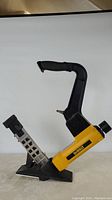 Side profile of the DeWALT pneumatic flooring nailer showing yellow body, black handle, nail magazine and base plate.
