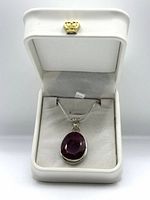 Ruby pendant displayed in white leatherette box with crown emblem.