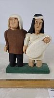 Full view of folk art carving showing a man, a woman holding a baby, and the baby figure, painted wooden sculpture on base.