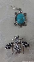 Turquoise turtle pendant with oval turquoise stone and silver-tone detailing, with bee brooch partially visible.