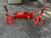 Front view of red hydraulic car jack with two matching red jack stands on pavement