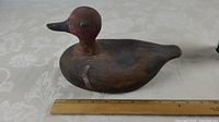 Side view of the wooden duck decoy showing its length against a ruler approximately 10 inches.