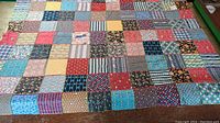 Full view of large colorful patchwork quilt laid flat showing varied vintage fabric squares in a grid.
