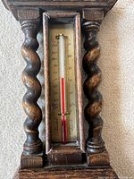 Close-up of the vintage thermometer showing temperature scale, glass tube, and carved wooden frame with barley twist columns