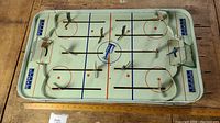 Top-down view of metal tabletop hockey game showing 10 player figures mounted on rods on the rink surface with painted game lines and a Stanley Cup logo at center.