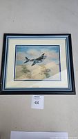Framed and matted canvas artwork showing an aircraft flying above clouds and land, placed face up.