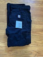 Folded navy blue Carhartt work pants showing Carhartt logo patch on back pocket and lot number tag