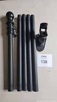Photo of the 5 black cylindrical flag pole sections with finial and clip, alongside the black metal mounting bracket and a lot number card.