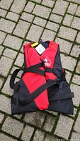 Full view of folded red and black life jacket showing straps and whistle attached