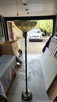 Full view of the tall antique floor lamp with Tiffany-style stained glass shade, placed indoors in a garage or storage room.