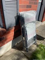 Four new Enduro folding chairs stacked and wrapped in plastic, leaning against a brick wall.