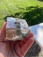 Calcite mineral specimen held in hand outdoors with clear translucent crystal structure and visible inclusions.