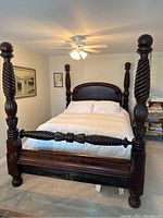 Front view of dark wood carved four-poster queen bed frame with bedding