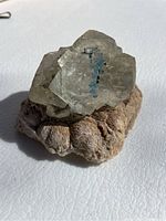 Close-up of pale green translucent fluorite crystal cluster on beige matrix.