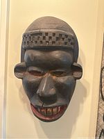 Front view of the black hand carved wooden tribal mask with checkerboard forehead and red-accented facial features.