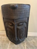 Front and angled views of a large black wooden tribal mask from Nigeria, showing detailed facial carvings and textured geometric patterns on the surface.