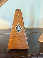 Front view of the wooden metronome with black diamond emblem and trident symbol.