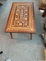 Rectangular coffee table showing the intricate mosaic wood top design with geometric wood inlay patterns in multiple wood tones and brass-capped tapered legs.