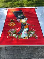 Full view of the red fabric wall hanging featuring the cartoon mouse design with flowers, laid flat on a table outdoors.