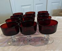 Front view of 12 ruby red champagne glasses arranged in rows, showing rich red bowls and clear stems.