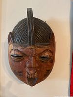 Front view showing facial features of the hand carved wooden tribal mask including closed eyes, lips with teeth, and cheek scarification marks.