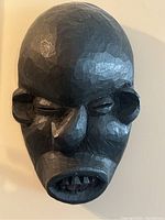 Front view of hand carved black wooden tribal mask showing unique twisted nose and uneven mouth with carved teeth.
