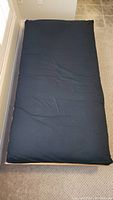 Top view of twin futon mattress with black cotton cover showing fabric and some creasing.