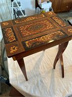 Full view of the vintage Italian music box table showing intricate marquetry top and standing on three legs, with one leg damaged.