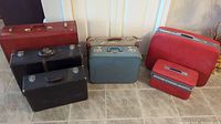 Photo showing six vintage suitcases of different colors and sizes on floor.