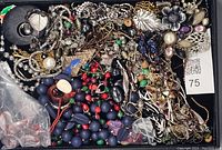 Top-down photo displaying a mixed lot of broken vintage costume jewelry pieces including blue and red beads, assorted chains, metal floral charms, and pendants with missing stones.