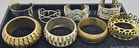 View of eight metal bracelets arranged in two rows showing different designs and styles.