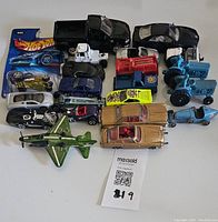 Top-down view of 21 vintage diecast and rubber toy vehicles including cars, trucks, tractors, and a model airplane. Items show varied colors and styles from different brands.