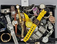 Top view of mixed lot of damaged watches in a black tray showing multiple colors and strap types