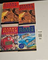 Four Harry Potter books on a white surface, showing front covers including 'Goblet of Fire' in both hardcover and softcover, 'Philosopher's Stone', and 'Chamber of Secrets'.