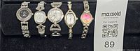 Photo of five ladies' wristwatches laid in a single row, showing watch faces and metal link bracelets.
