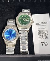 Pair of two men's wristwatches, one with a green dial and day-date window and one with a blue dial and compass bezel markings.