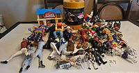 Wide view of assorted soldier and action figure toys laid out on table, showing variety of sizes and styles including fabric and plastic figures.