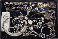 Top-down view of mixed vintage costume jewelry including silver-tone crescent pendant necklace, black and white bead necklace, blue oval faux stone necklace with pearls, various chains, bracelets, and earrings.