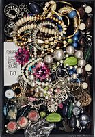 Top-down close view of assorted vintage jewelry showing numerous bracelets, earrings, necklaces, and decorative pieces inside a black tray.