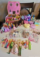 Full view of the lot showing Disney Princess dolls standing, several compact cases, pony figures, and small toys arranged in front of a pink house-shaped compact