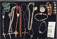 Top view of religious jewelry lot displaying rosaries, crosses, chains, medals, and bracelets all laid in a dark display tray.