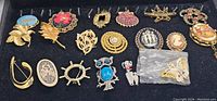 Full view of collection of vintage brooches and pendants arranged in black tray