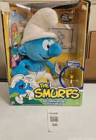 Front view of the Smurfs 50th Anniversary plush figure in original box showing main plush doll and exclusive gold figurine sticker.