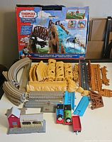 Full view of the Thomas & Friends Trackmaster Action Canyon set components spread out with original box behind, showing track pieces, terrain parts, bridges, and trains.