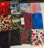 Top view of 12 women's scarves neatly folded showing various colors and patterns including floral, animal print, stripes, and abstract designs.