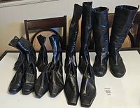 Overview of six pairs of black women's shoes and boots arranged on table, showing variety of styles and square toe shapes