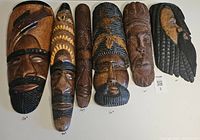 Full view of all seven hand-carved wooden masks, laid flat, showing size variations and design differences